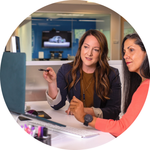 Two business women talking about sales in office at desk with laptop